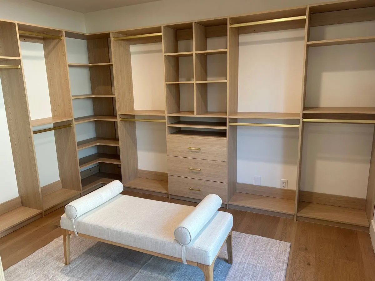 Natural oak walk-in closet with bench and gold hardware