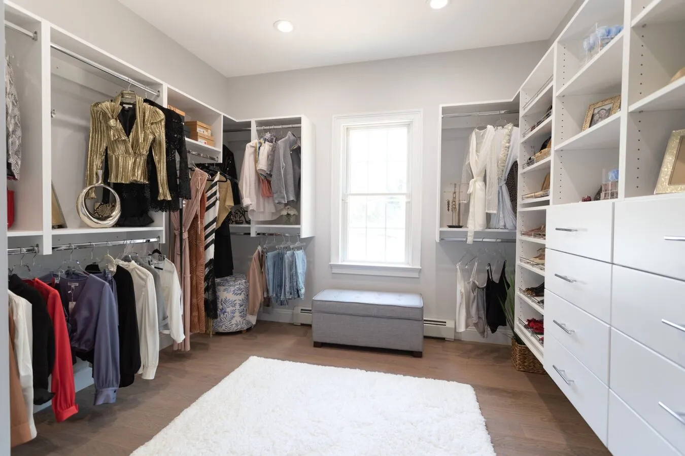 Large white walk-in closet room with hardwood floors and ottoman